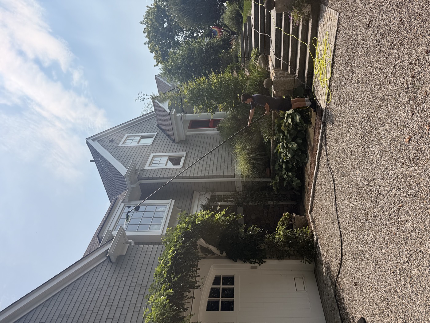 Clear View technician cleaning second-storey windows of a gray shingle Connecticut home with a water-fed pole