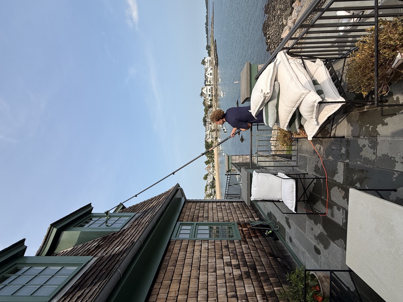 Clear View technician cleaning upper windows from a waterfront terrace overlooking the harbor, Connecticut