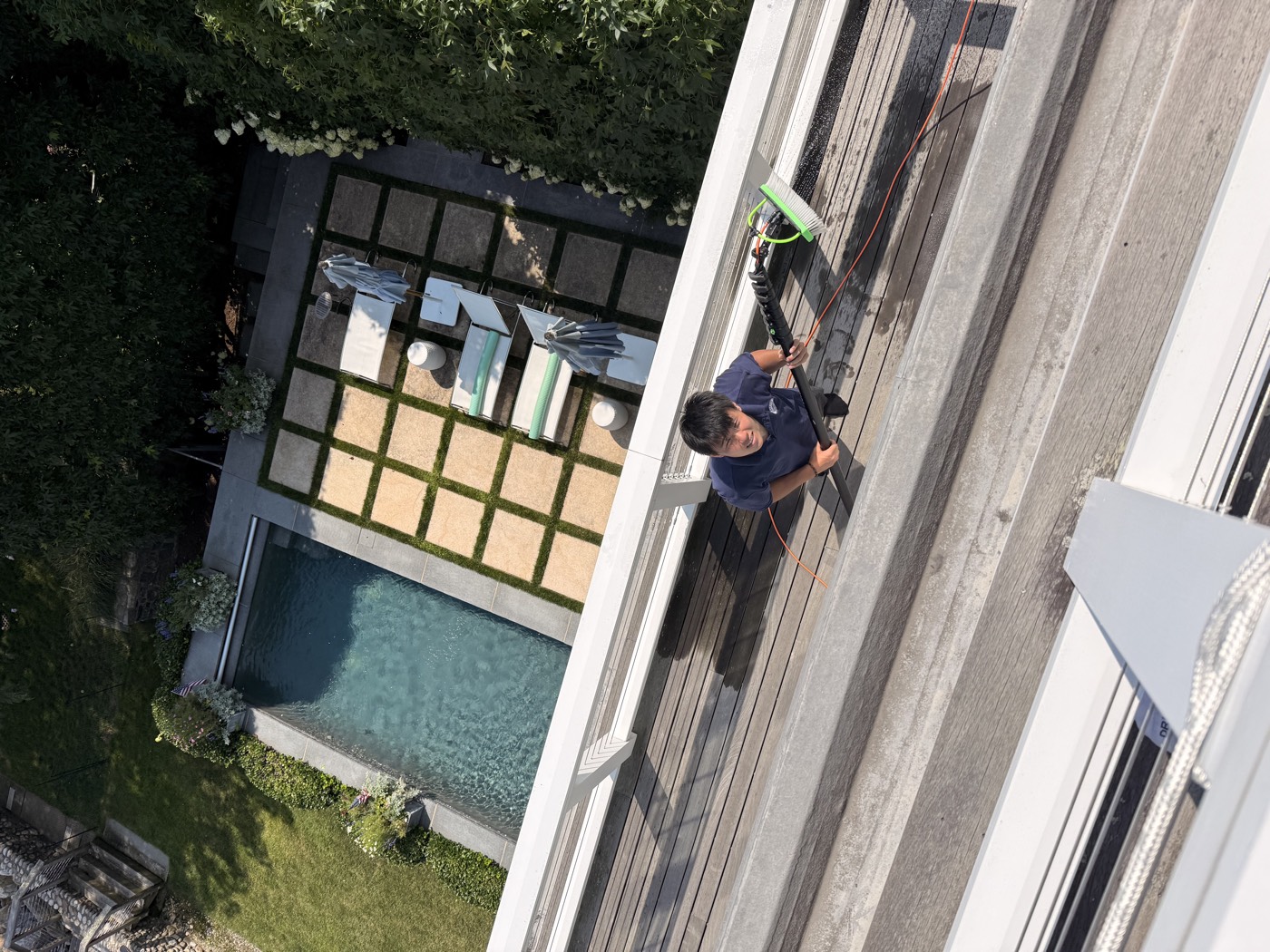 Overhead view of a Clear View technician cleaning windows above a poolside terrace in Connecticut